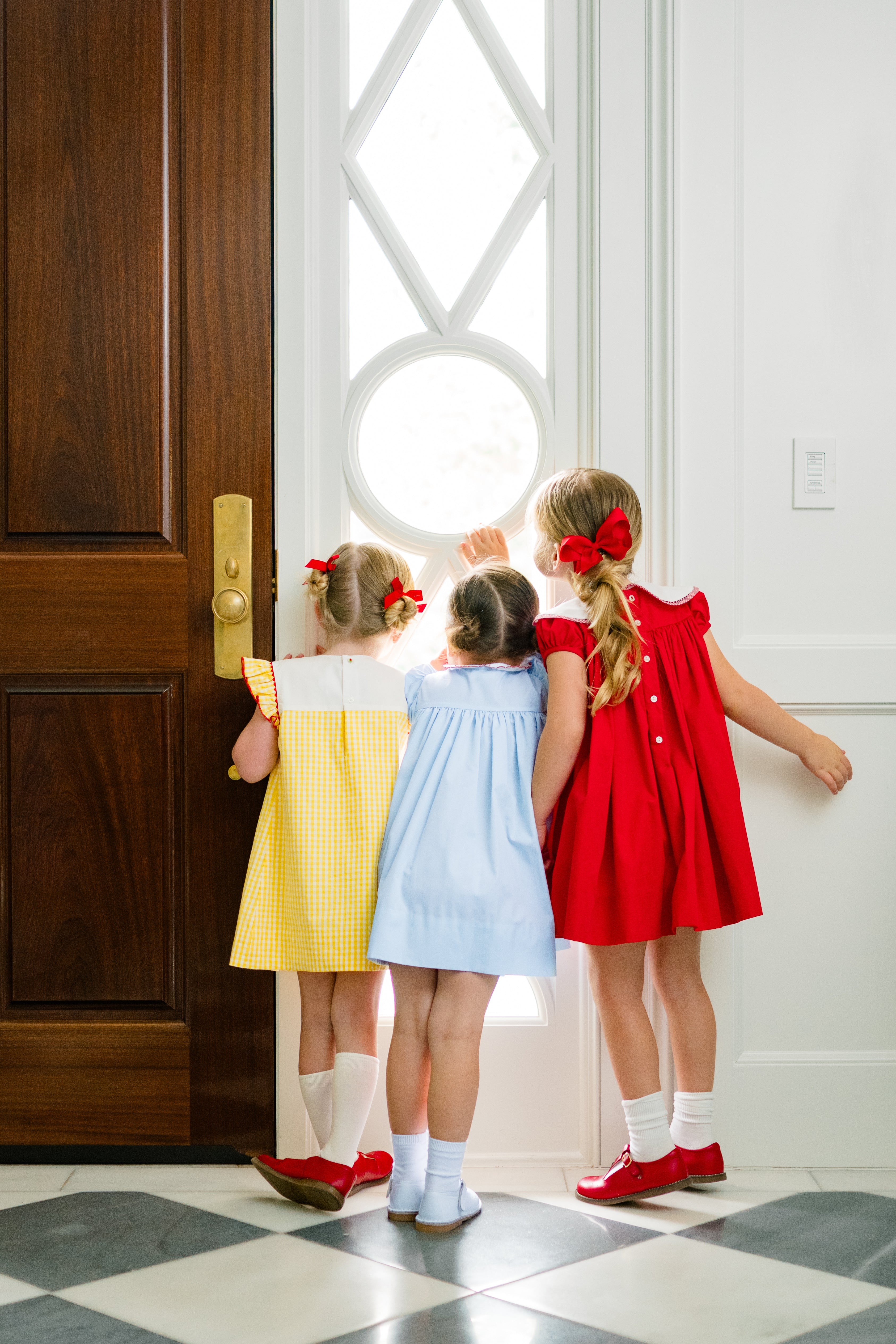 Three children in colorful dresses standing in front of a door.